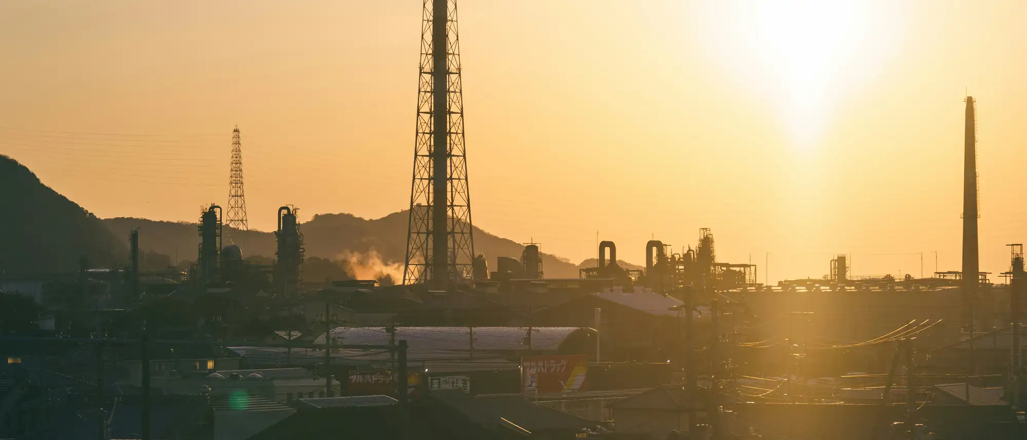 Industrial plant with tall stacks silhouetted against a warm orange evening sky