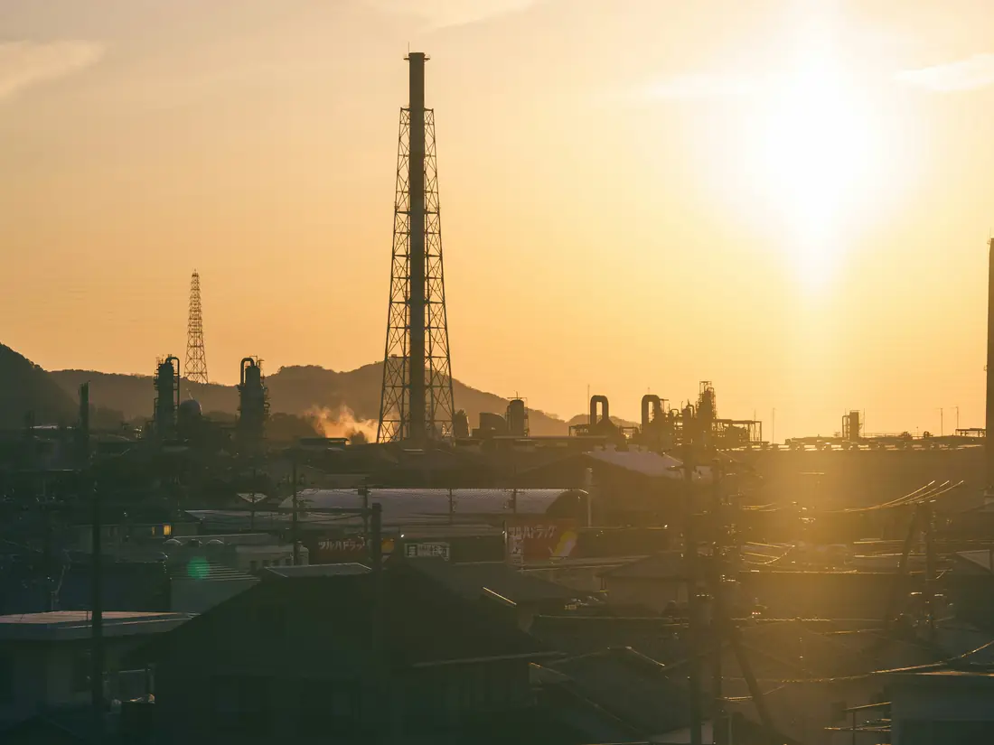Industrial plant with tall stacks silhouetted against a warm orange evening sky
